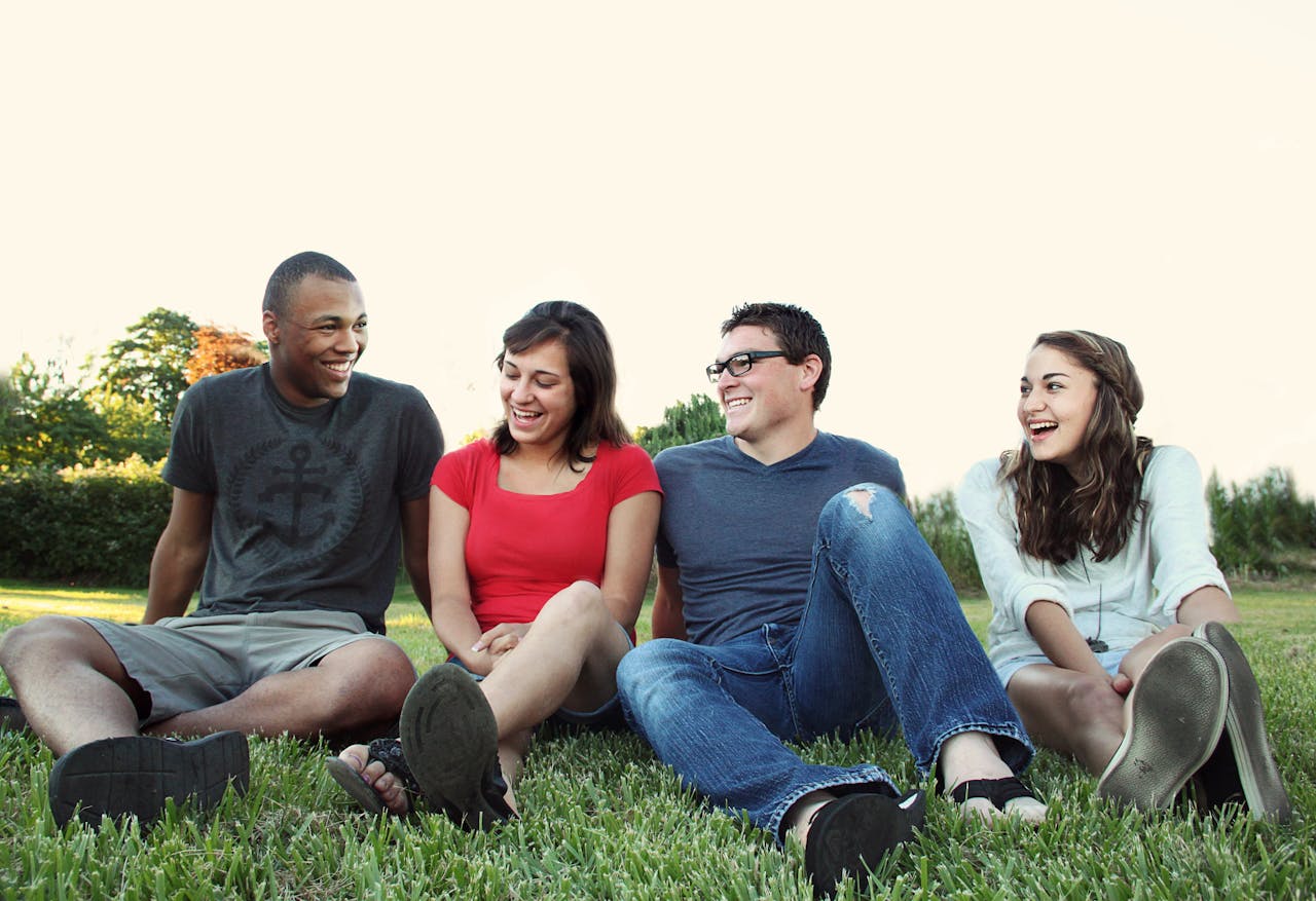 Mastering the First Impression: Your intriguing post title goes here A group of young adults smiling while sitting on grass in a sunny park, enjoying friendship and leisure.