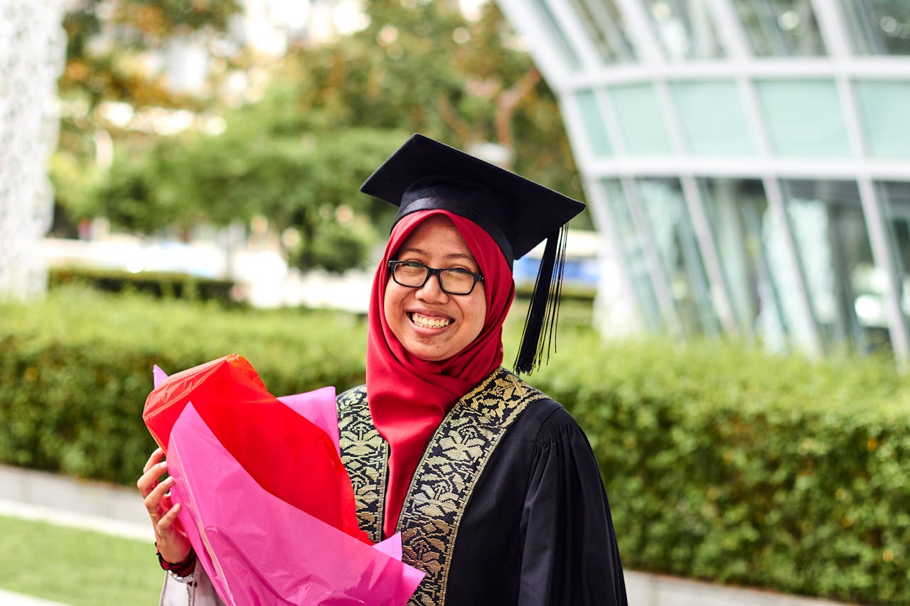 about-img-01 A proud female graduate in hijab with flowers celebrates her achievement outdoors.