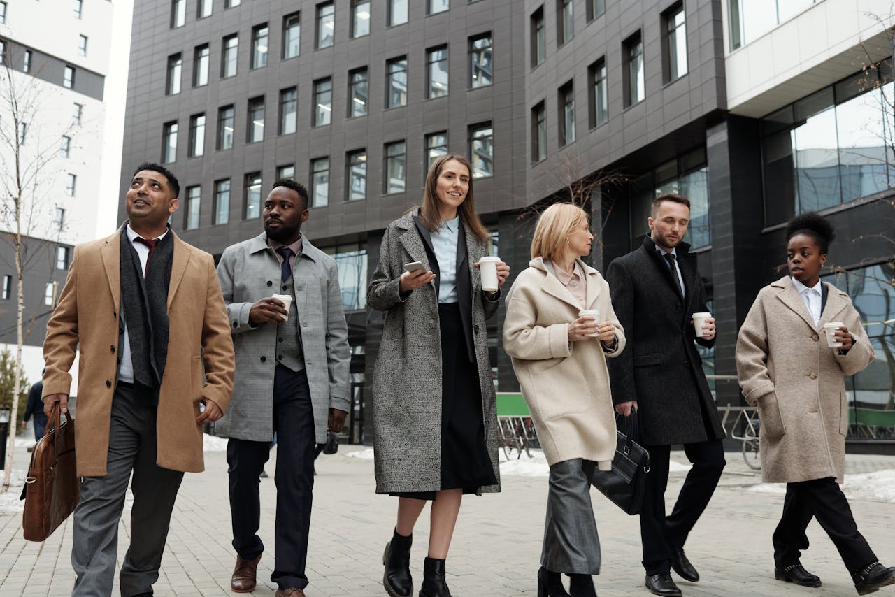 about-img A diverse group of business professionals walking outdoors with coffee cups, showcasing teamwork.