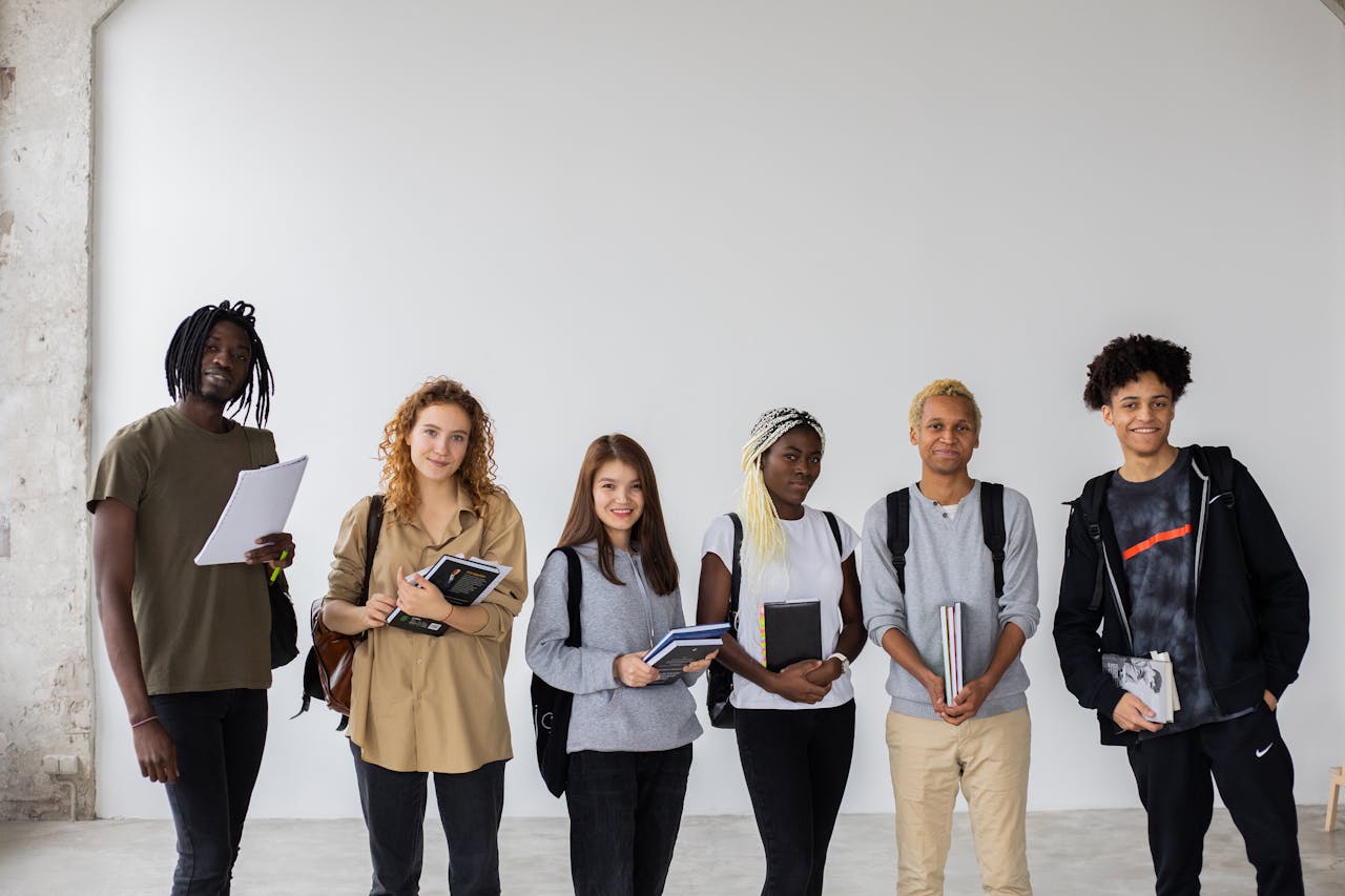 our-story Group of diverse young multiracial classmates with notebooks and textbooks and backpacks smiling at camera