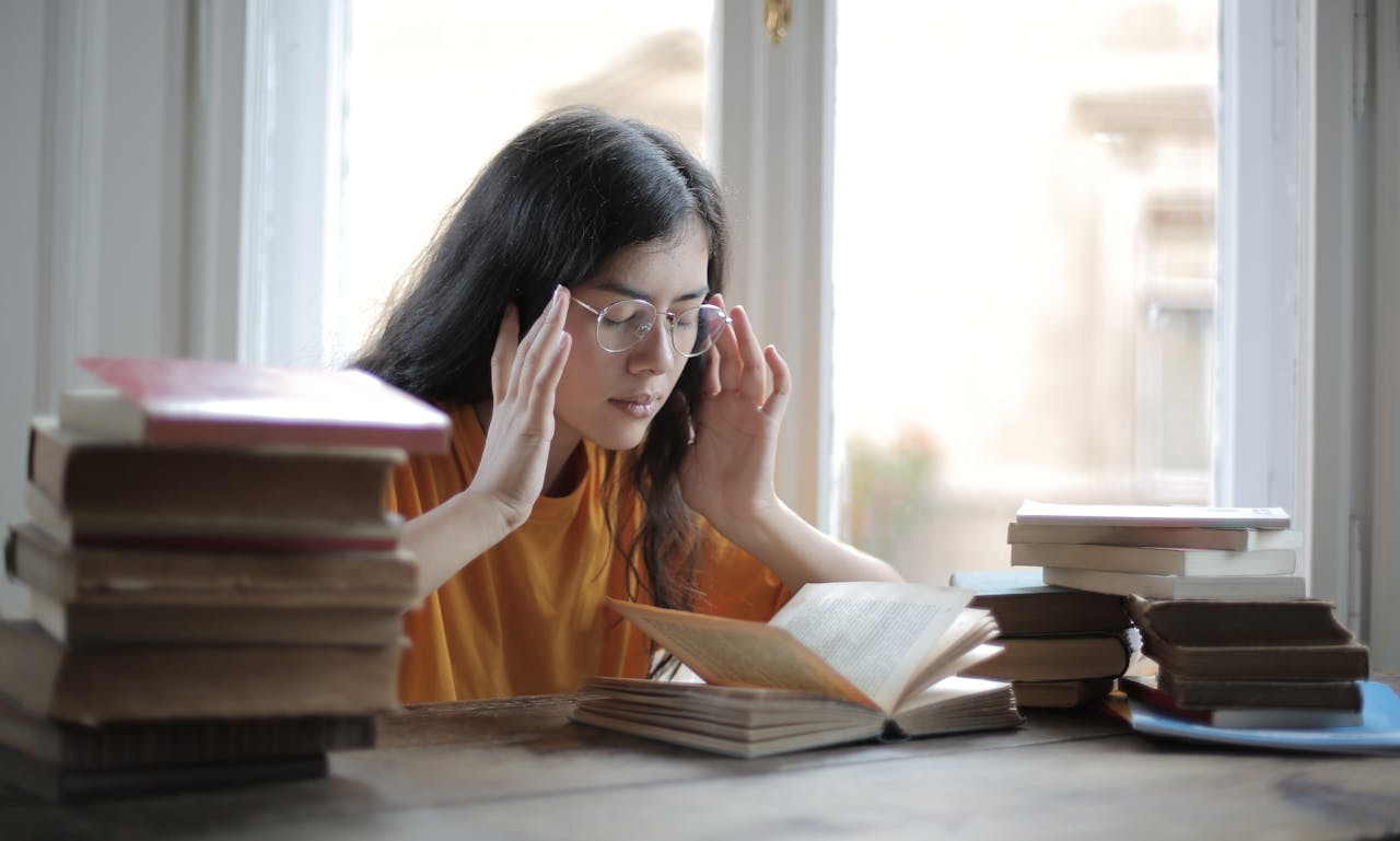 A young woman feeling fatigued while reading and studying surrounded by books.