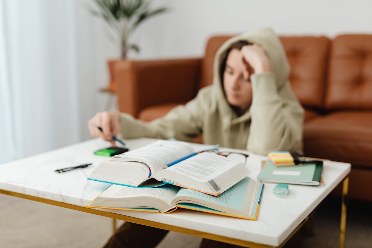 Teenager focused on studying with open books and notes on a living room table, capturing a study session.