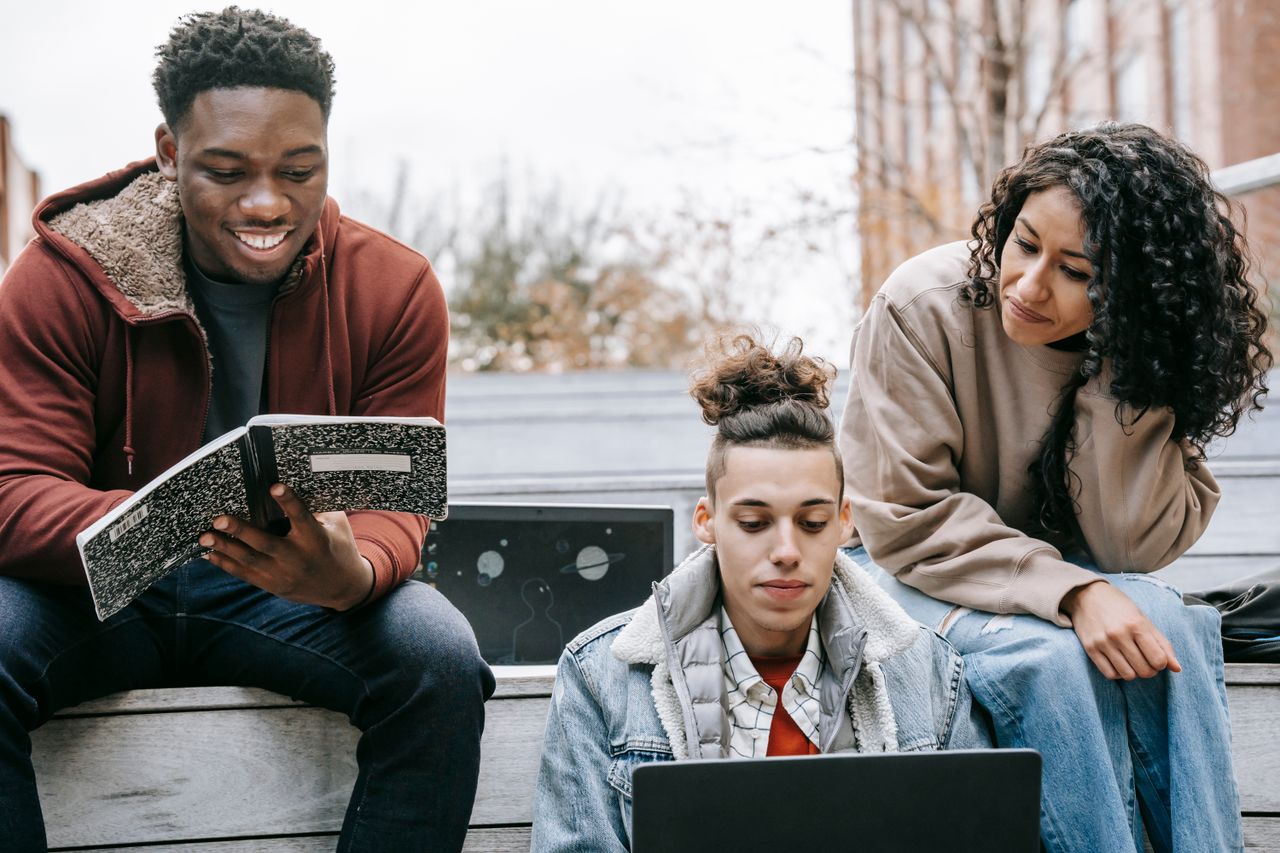 contact-header Group of multiethnic happy young students doing homework with copybook and netbook on street