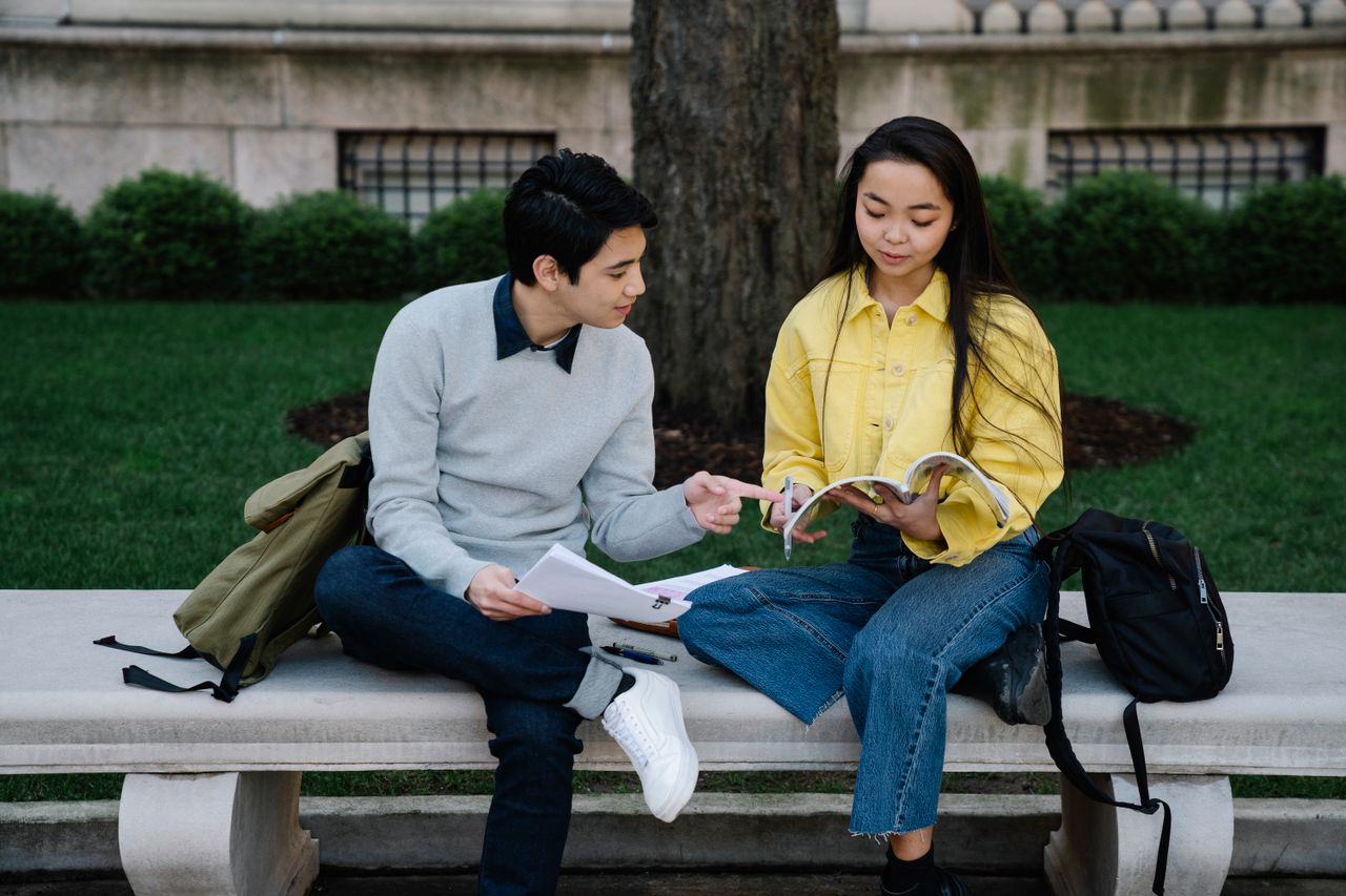 project-01-a Two students studying together outdoors on a concrete bench with books and backpacks.