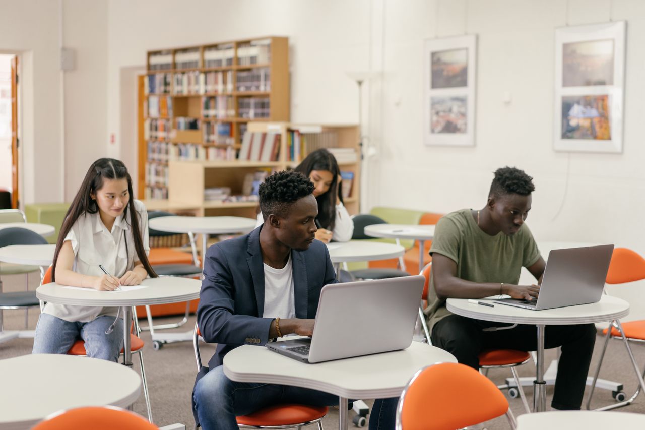 Students focused on laptops and notes in a bright classroom setting.