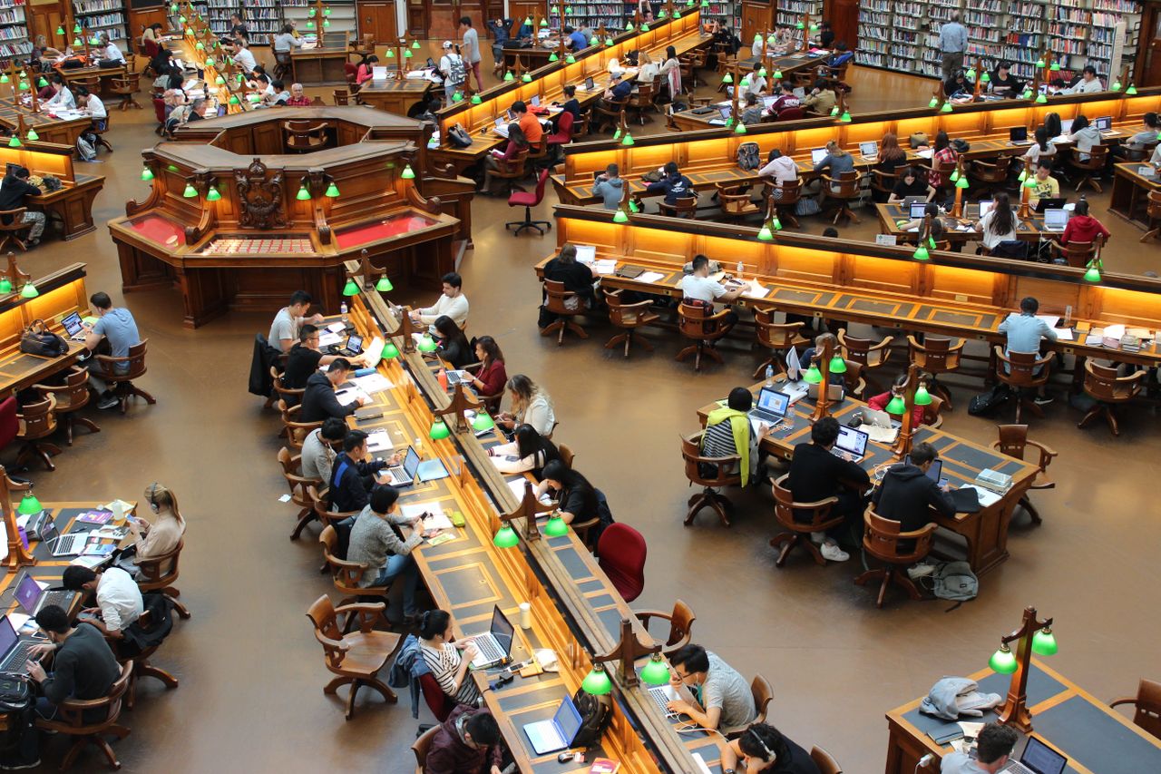 gallery-01 A lively university library scene with students studying diligently at wooden desks.