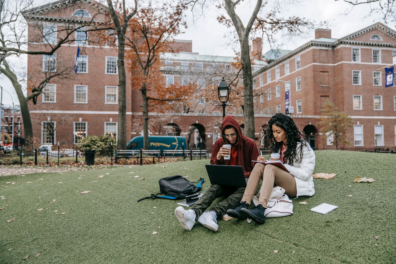 about-me-01 College students studying with laptops and books in a park during fall.