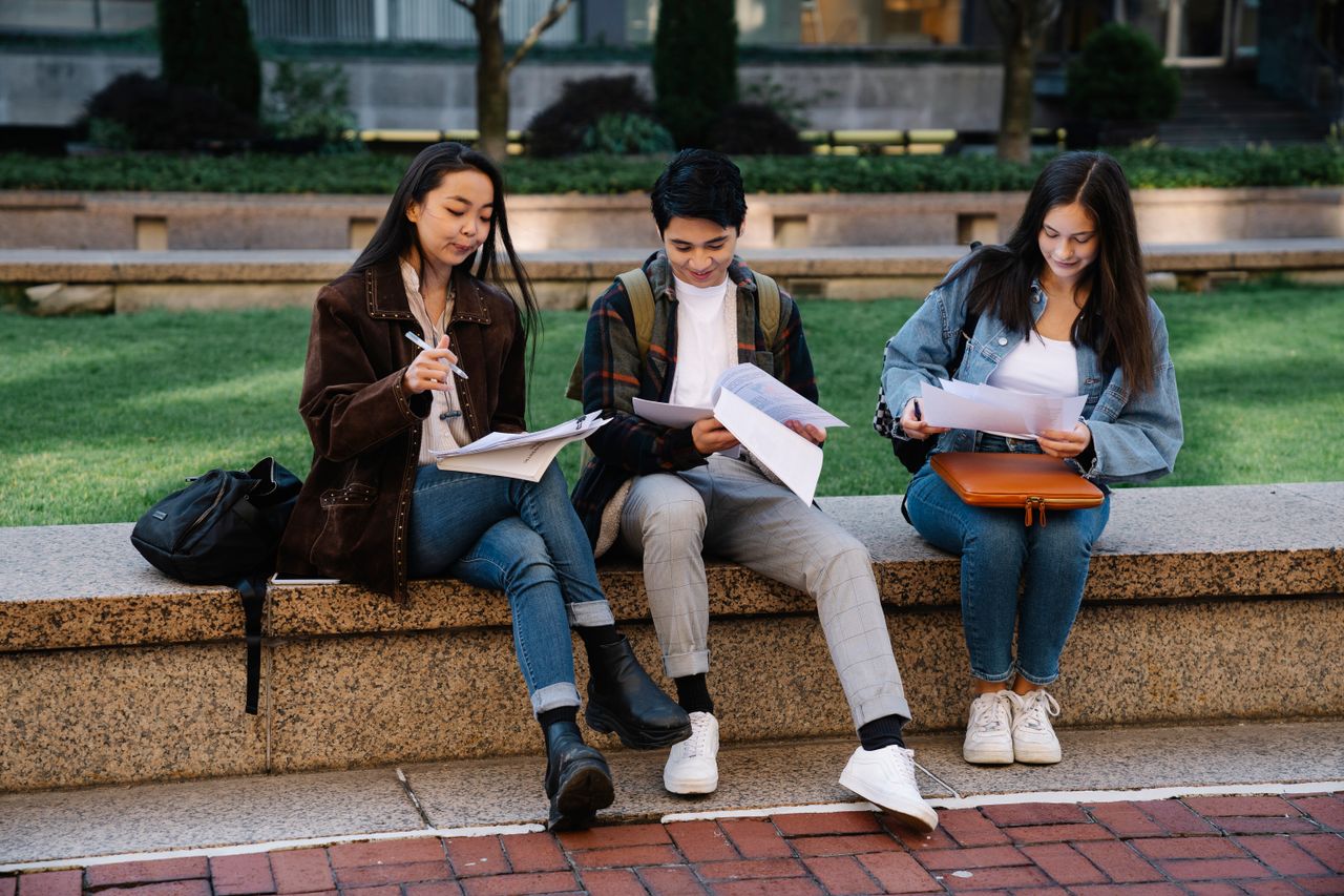 services-03 Three students studying together on a bench in a university campus setting outdoors.